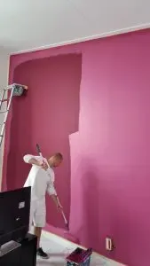 Behanger schildert een muur met roze latex verf, zichtbaar in actie.